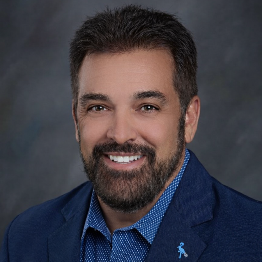 Smiling man in a blue suit jacket and blue shirt against a gray background.