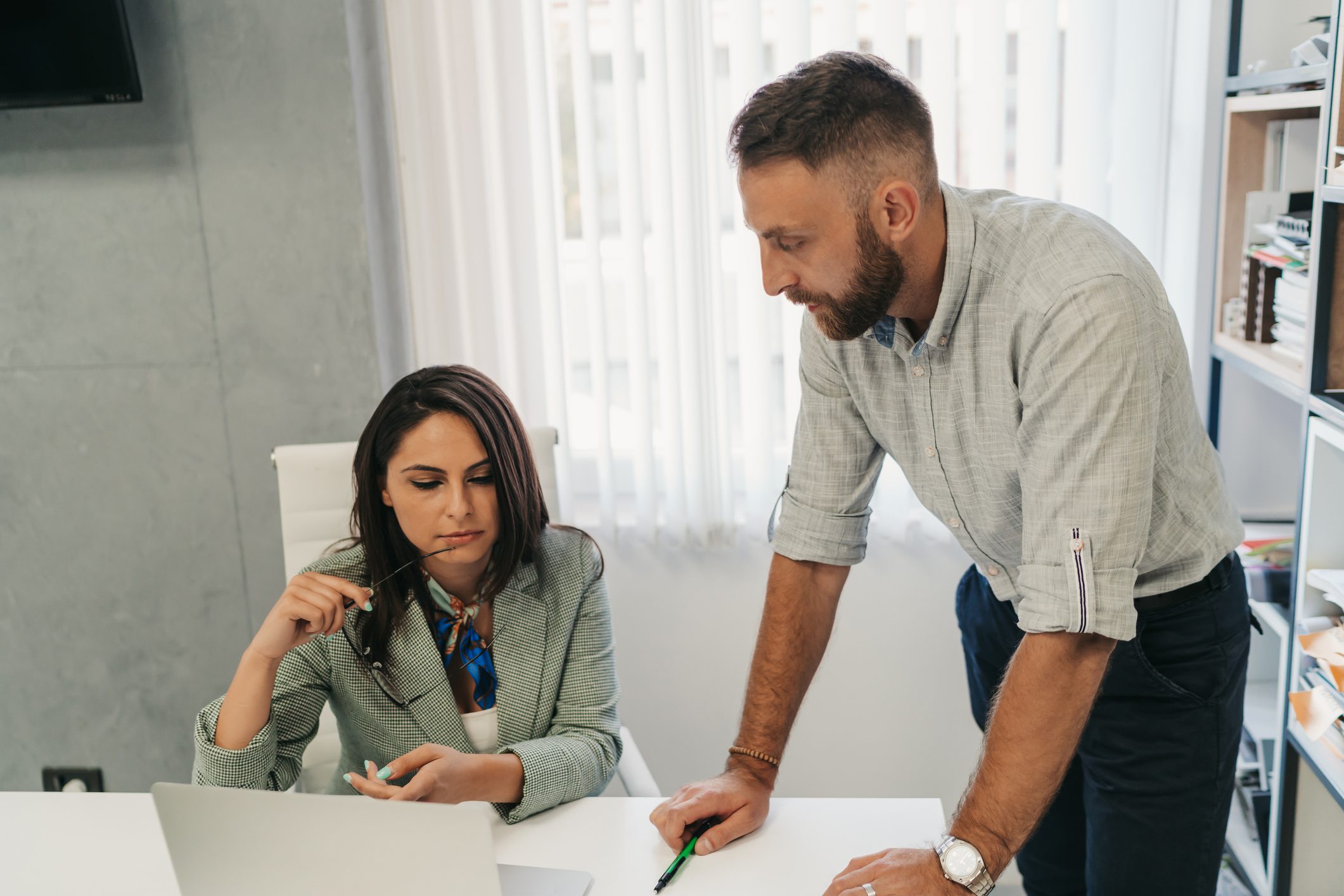A man and woman discussing work at a desk with a laptop.
